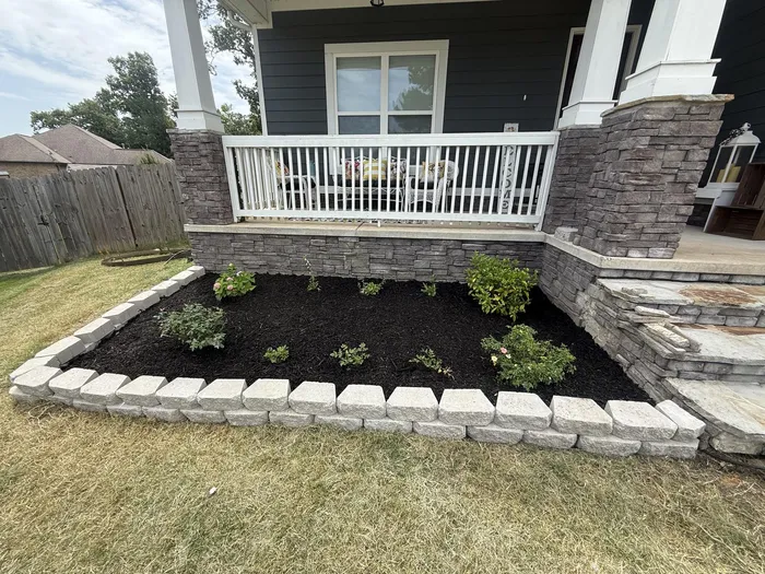 Rebuilt porch-side bed with stone border, dark mulch, and fresh shade plantings