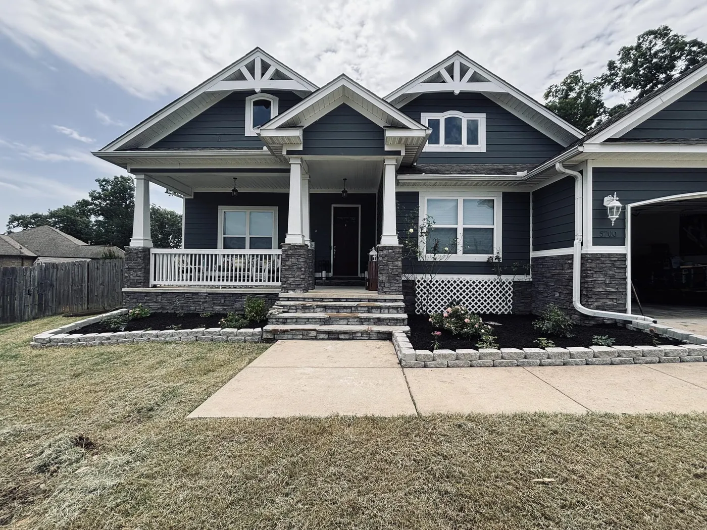 Craftsman home with new white gable brackets and rebuilt front flower beds with stone borders and black mulch