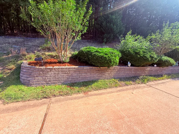 Stacked-stone garden bed with fresh red mulch along the driveway